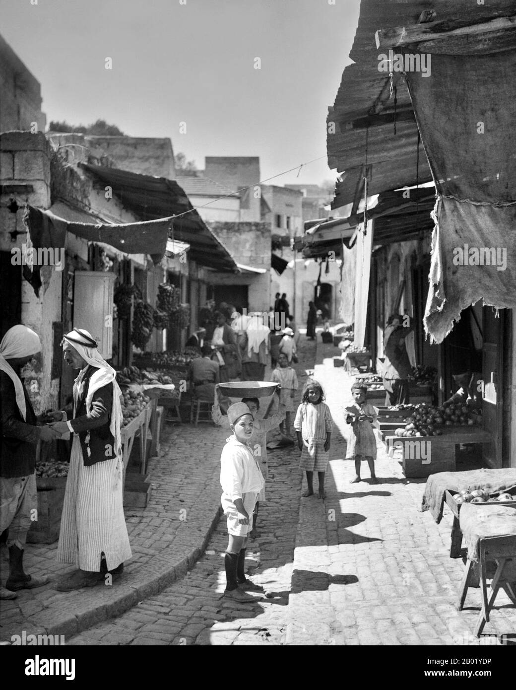 Palestine : hommes et enfants palestiniens au bazar de Nazareth, v. 1934-1937. Palestine est un nom donné à la région géographique entre la mer Méditerranée et le Jourdain. La région est également connue comme la Terre d'Israël, la Terre Sainte et le Levant Sud. En 1832, la Palestine a été conquise par l'Égypte de Muhammad Ali, mais en 1840, la Grande-Bretagne est intervenue et a rendu le contrôle du Levant aux Ottomans en échange de nouvelles capitulations. La fin du XIXe siècle voit le début de l'immigration sioniste et la renaissance de la langue hébraïque. Banque D'Images