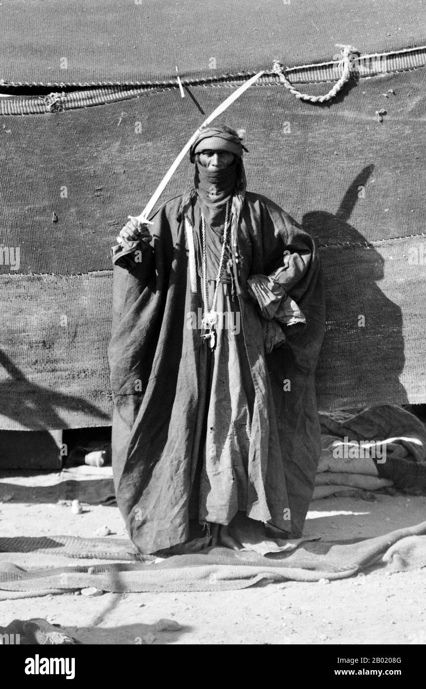 Arabie : femme bédouine tenant l'épée pour la danse de l'épée, v. 1898-1914. Les Bédouins font partie d'un groupe ethnique arabe vivant principalement dans le désert, traditionnellement divisé en tribus, ou clans, connu en arabe sous le nom de ʿašāʾir. Le terme bédouin dérive d'une forme plurielle du mot arabe badawī, tel qu'il est prononcé dans les dialectes familiers. Le terme arabe badawī dérive du mot bādiyah, qui signifie désert semi-aride (par opposition à ṣaḥarāʾ qui signifie désert). À partir de la fin du XIXe siècle, de nombreux Bédouins sous domination britannique ont commencé à transiter vers une vie séminomadique. Banque D'Images