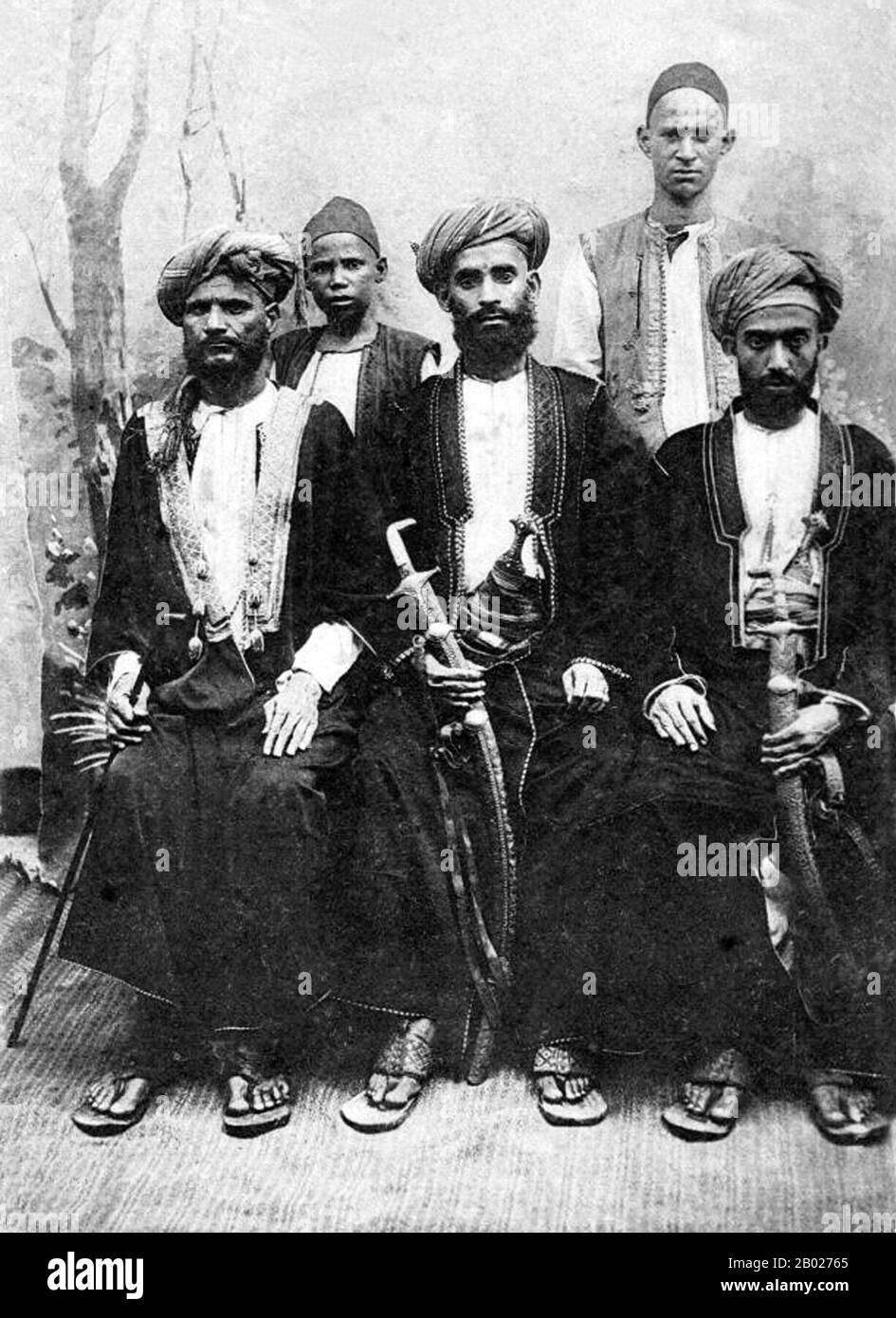 Tanzanie/Zanzibar : hommes arabes omanais de substance avec deux serviteurs. Photo des frères Coutinho, v. 1903-1911. Zanzibar est une partie semi-autonome de la Tanzanie en Afrique de l'est. Il est composé de l'archipel de Zanzibar dans l'océan Indien, à 25-50 km (16-31 mi) au large des côtes du continent, et se compose de nombreuses petites îles et deux grandes : Unguja (l'île principale, appelée officieusement Zanzibar), et Pemba. La capitale de Zanzibar, située sur l'île d'Unguja, est la ville de Zanzibar. Son centre historique, connu sous le nom de Stone Town, est un site du patrimoine mondial. Banque D'Images