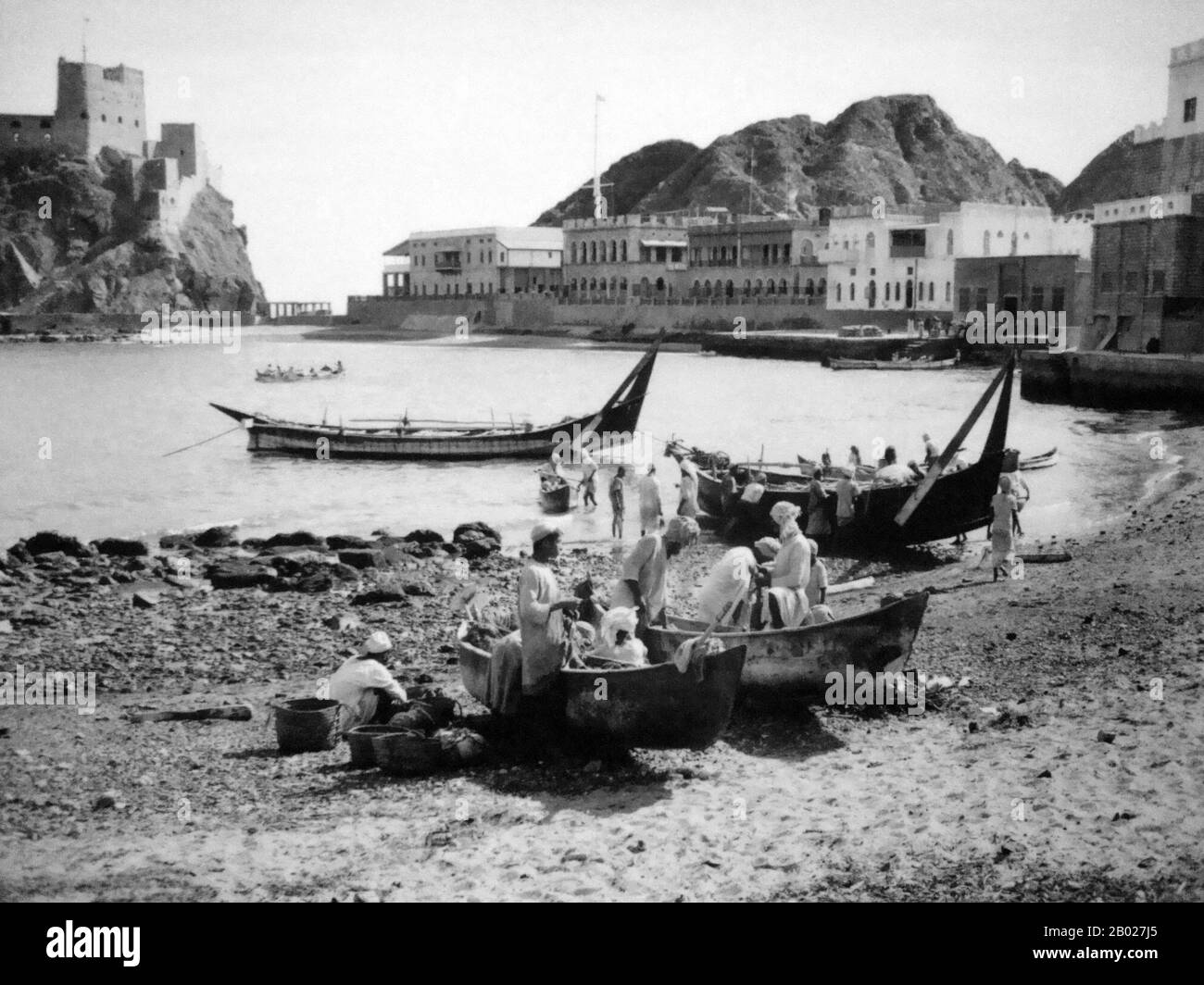 Oman : 'Badans' et 'Houris' (boutres traditionnels) arrivent à la plage de Muscat en face de l'ancien palais Al Alam, mai 1957. Un boutre est un voilier arabe traditionnel avec une ou plusieurs voiles lateen. Il est principalement utilisé pour transporter des objets lourds, comme des fruits, le long des côtes de la péninsule arabique, du Pakistan, de l'Inde et de l'Afrique de l'est. Les grands boudins ont des équipages d'environ trente personnes, tandis que les petits boudins ont généralement des équipages d'environ douze personnes. Jusqu'à nos jours, les dhows effectuent des voyages commerciaux entre le golfe arabe ou le golfe Persique et l'Afrique de l'est en utilisant les voiles comme seul moyen de propulsion. Banque D'Images