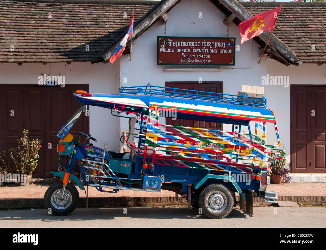 Laos : un jamboh (jumbo) garé devant le bureau de police sur Sisavangvong Road, Luang Prabang. Le « jumbo » est un taxi à trois roues et est le moyen de transport courant dans les grandes villes du Laos. Ce sont des motos modifiées avec deux bancs couverts à l'arrière qui assistent environ six personnes assez confortablement. Luang Prabang était autrefois la capitale d'un Royaume du même nom. Jusqu'à la prise de pouvoir communiste en 1975, elle était la capitale royale et le siège du gouvernement du Royaume du Laos. La ville est aujourd'hui classée au patrimoine mondial de l'UNESCO. Banque D'Images