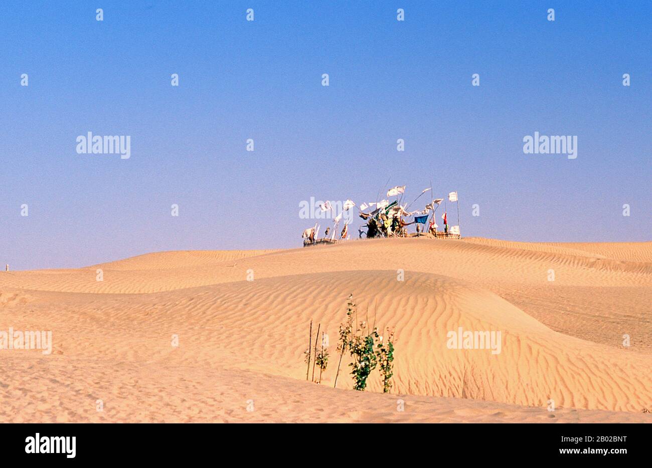 Chine : un tombeau avec des drapeaux un flottant plane sur les dunes de sable près de l'Imam Asim Mazar (sanctuaire) dans le désert près de Khotan, province du Xinjiang. Le sanctuaire de l'Imam Asim et d'autres tombes se trouvent à 23 kilomètres de Khotan (Hotan) sur la route de la soie au sud. C'est le site d'un immense pèlerinage chaque mois de mai. L’Imam Asim a été l’un des premiers missionnaires islamiques à visiter cette région. Khotan retrace son histoire au moins aussi loin que le IIIe siècle av. J.-C., lorsque le fils aîné de l'empereur indien Asoka s'est installé ici. Banque D'Images