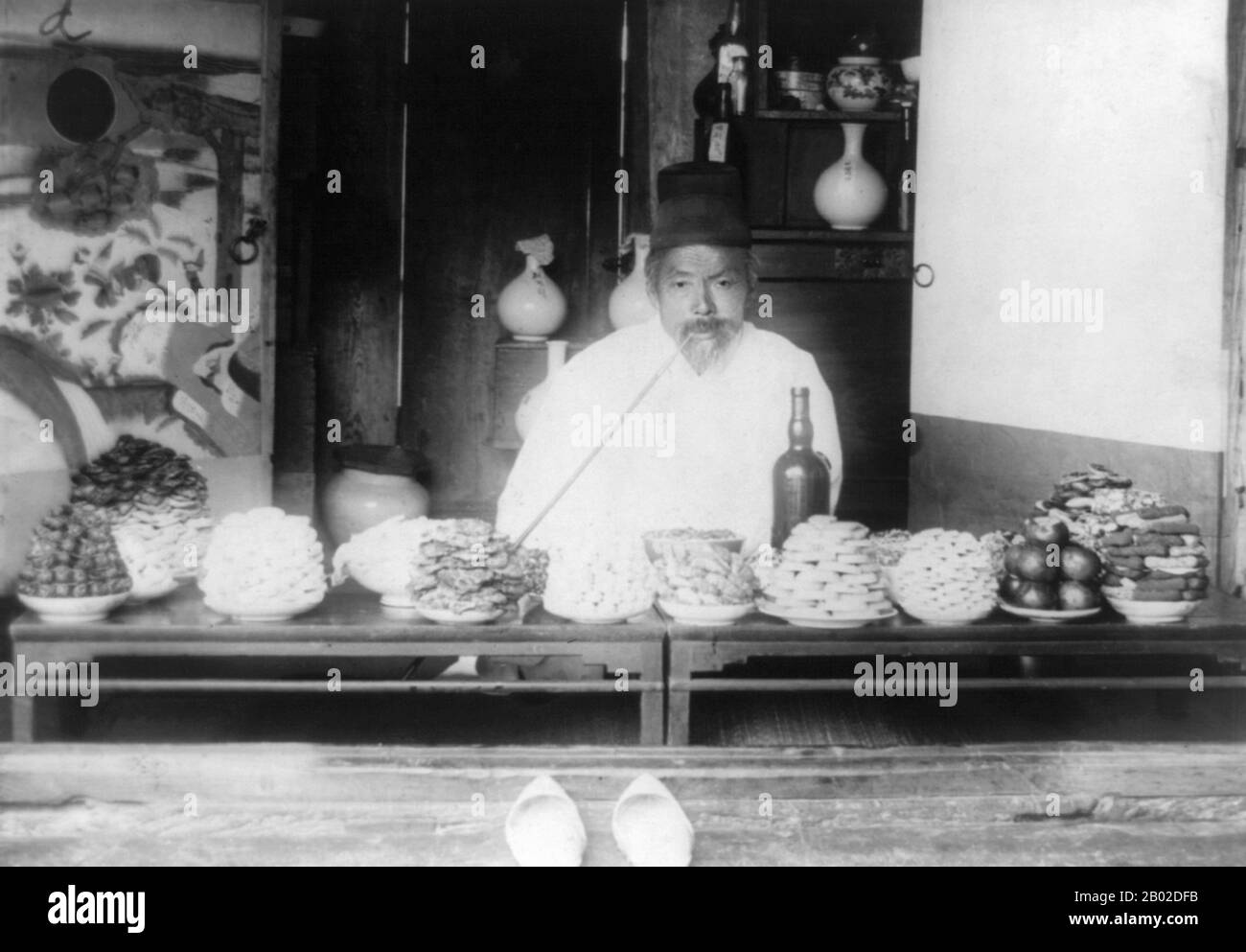 Corée : un marchand de Séoul fumant une longue pipe tout en vendant des liqueurs, des vins et des bonbons, v. 1890-1923. Séoul est la capitale et la plus grande métropole de la Corée du Sud. Mégapole avec une population de plus de 10 millions d'habitants, c'est la plus grande ville proprement dite du monde développé. La région de la capitale de Séoul, qui comprend la métropole environnante d'Incheon et la province de Gyeonggi, est la deuxième plus grande région métropolitaine du monde avec plus de 25,6 millions d'habitants, qui abrite plus de la moitié des Sud-Coréens et 632 000 résidents internationaux. Banque D'Images