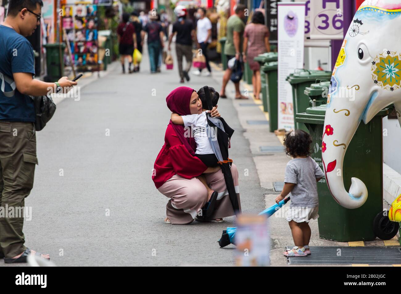 Une mère musulmane malais dans le hijab rouge s'est emparée pour embrasser son enfant dans la rue. Singapour. Banque D'Images