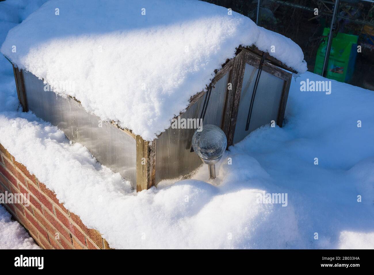 La chute de neige ajoute une protection thermique à un cadre froid placé sur un semoir en briques surélevées dans un jardin anglais en hiver Banque D'Images