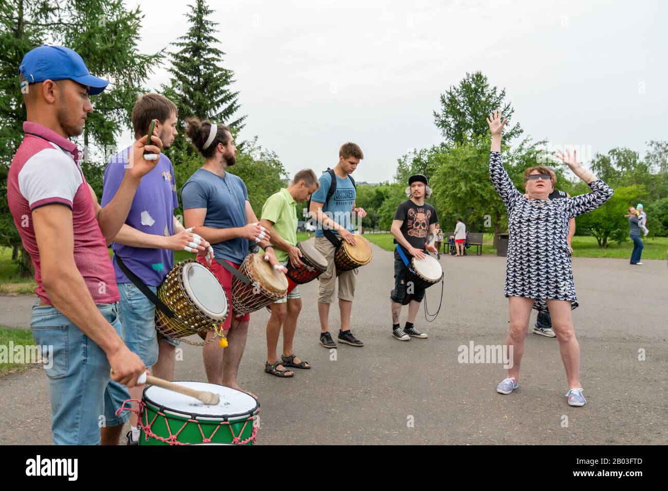 Krasnoyarsk, Russie, 30 juin 2019: Femme adulte drôle dansant devant des hommes jouant à la batterie africaine Tam Tam djembe dans un parc public en été. Banque D'Images