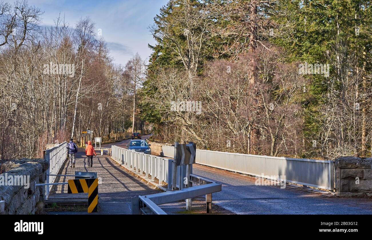 CARRON VILLAGE MORAY ECOSSE MARCHEURS ET VOITURE SUR LA ROUTE UNIQUE CARRON ET VIEUX PONT FERROVIAIRE QUI TRAVERSE LA RIVIÈRE SPEY Banque D'Images