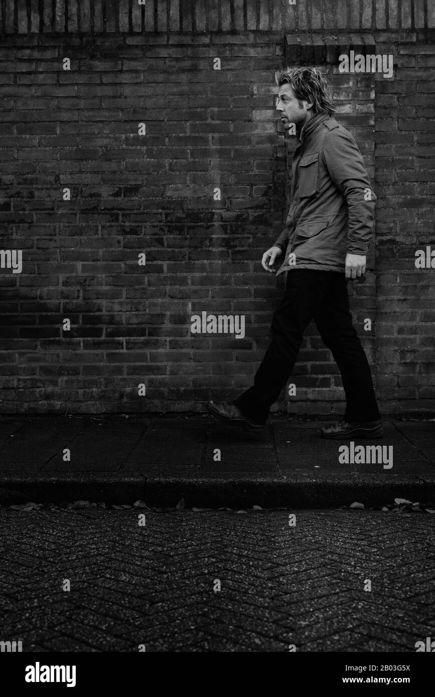 Homme en veste marchant sur le pavé le long du mur de briques. Banque D'Images