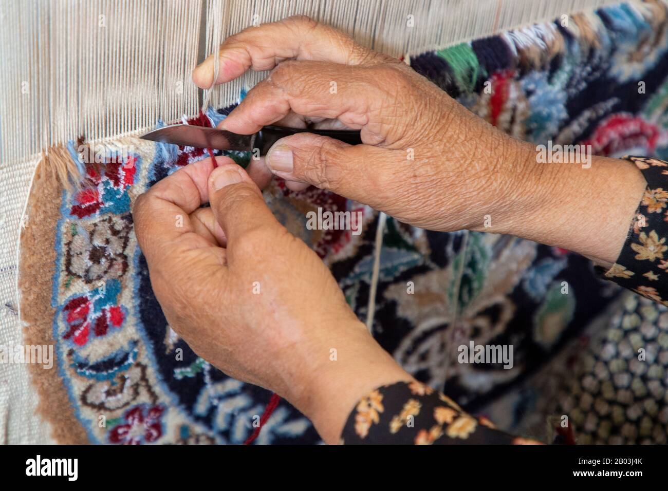 Femme a les mains de couper les fils dans le tissage de tapis, Iran Banque D'Images