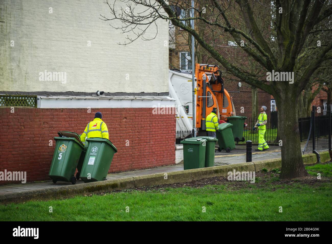 Un groupe d'hommes de poubelles qui tirent des poubelles de recyclage pour les charger sur un camion à ordures ou un camion à ordures Banque D'Images