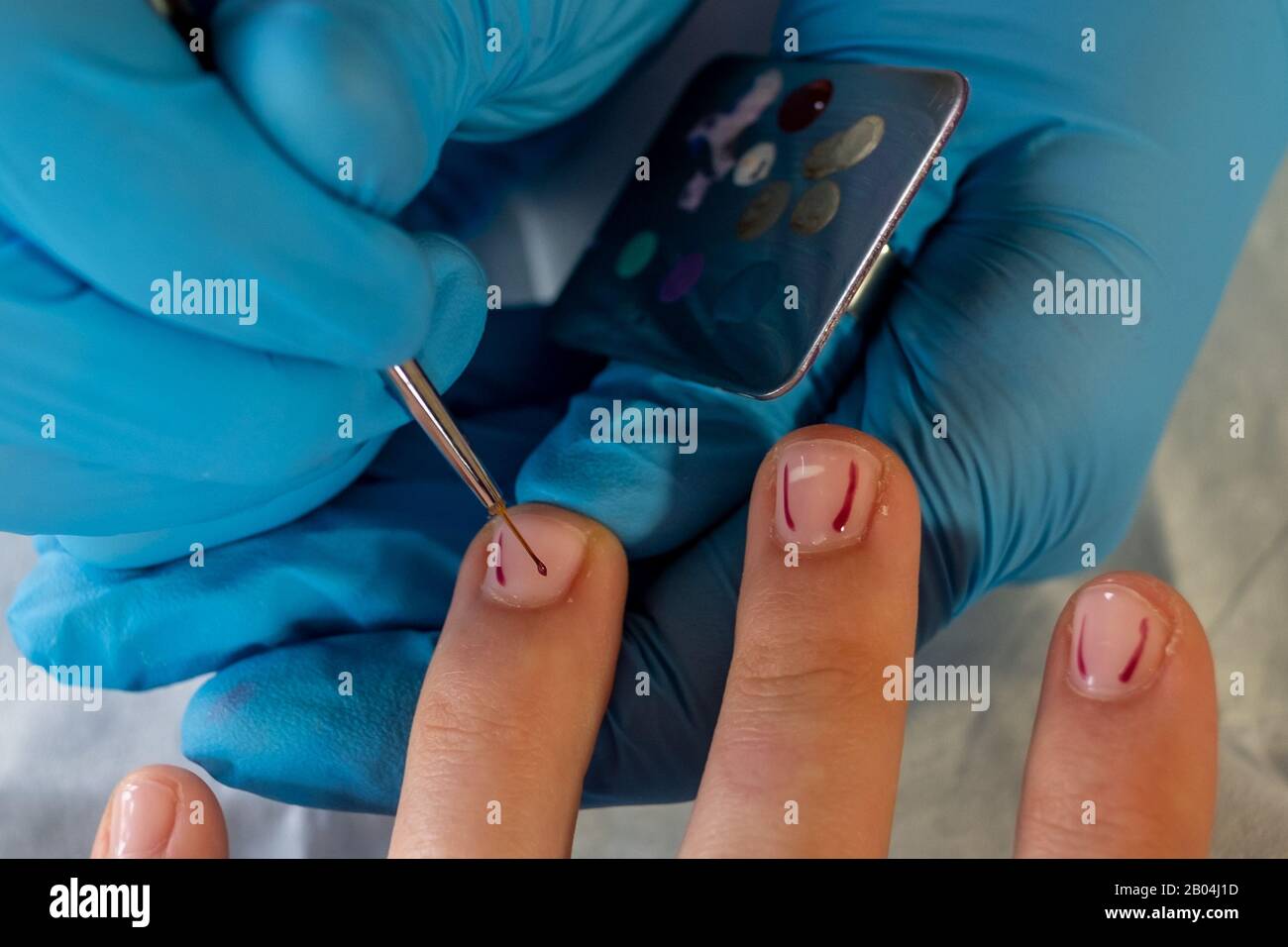 Gros plan de l'artiste de l'ongle ajoutant des points à la conception sur les ongles courts de la jeune femme. Banque D'Images