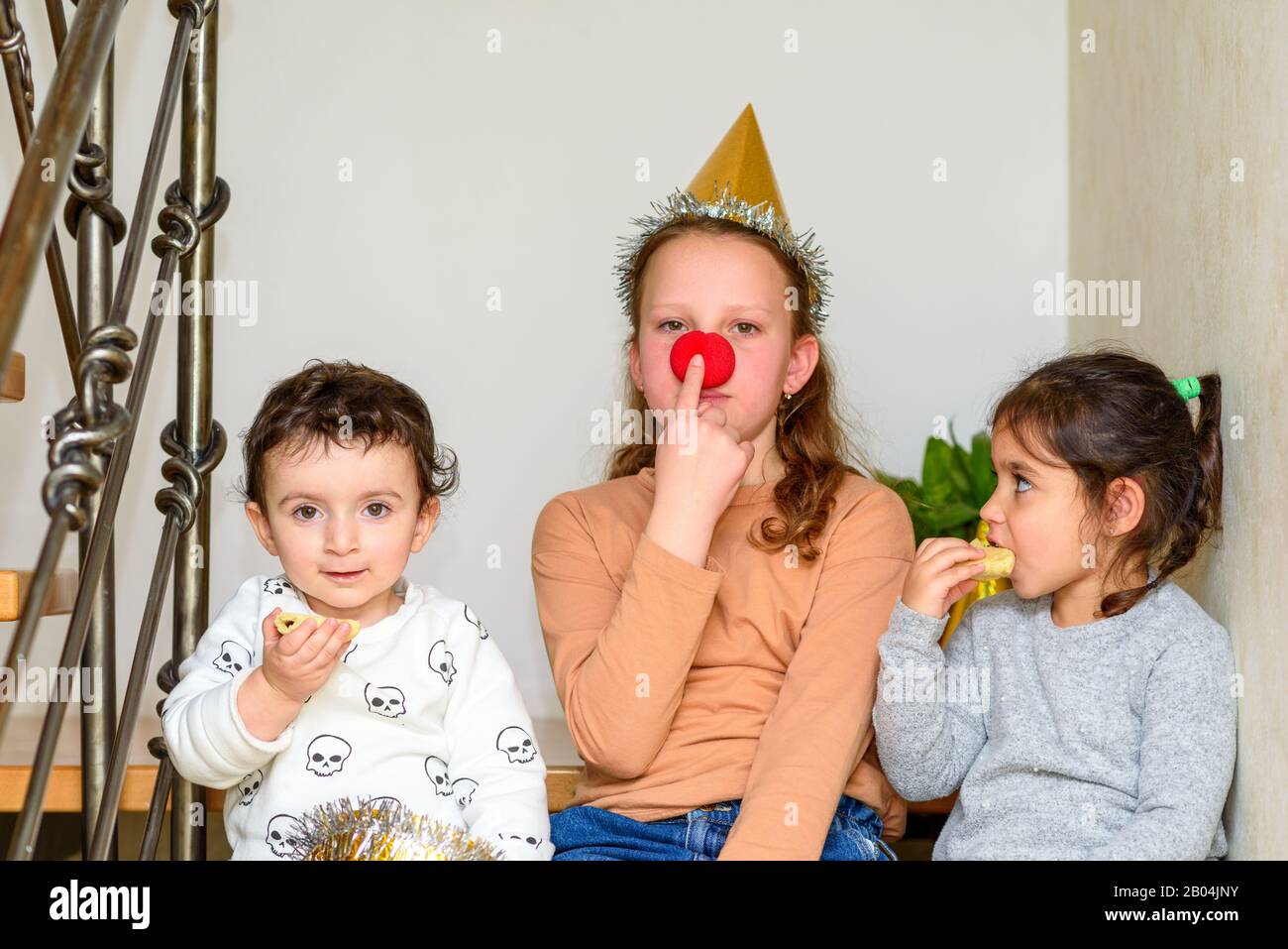 Portrait d'une adolescente avec un nez clown s'amuser avec de petits enfants mangeant des cookies sur le Purim ou la fête d'anniversaire. Banque D'Images