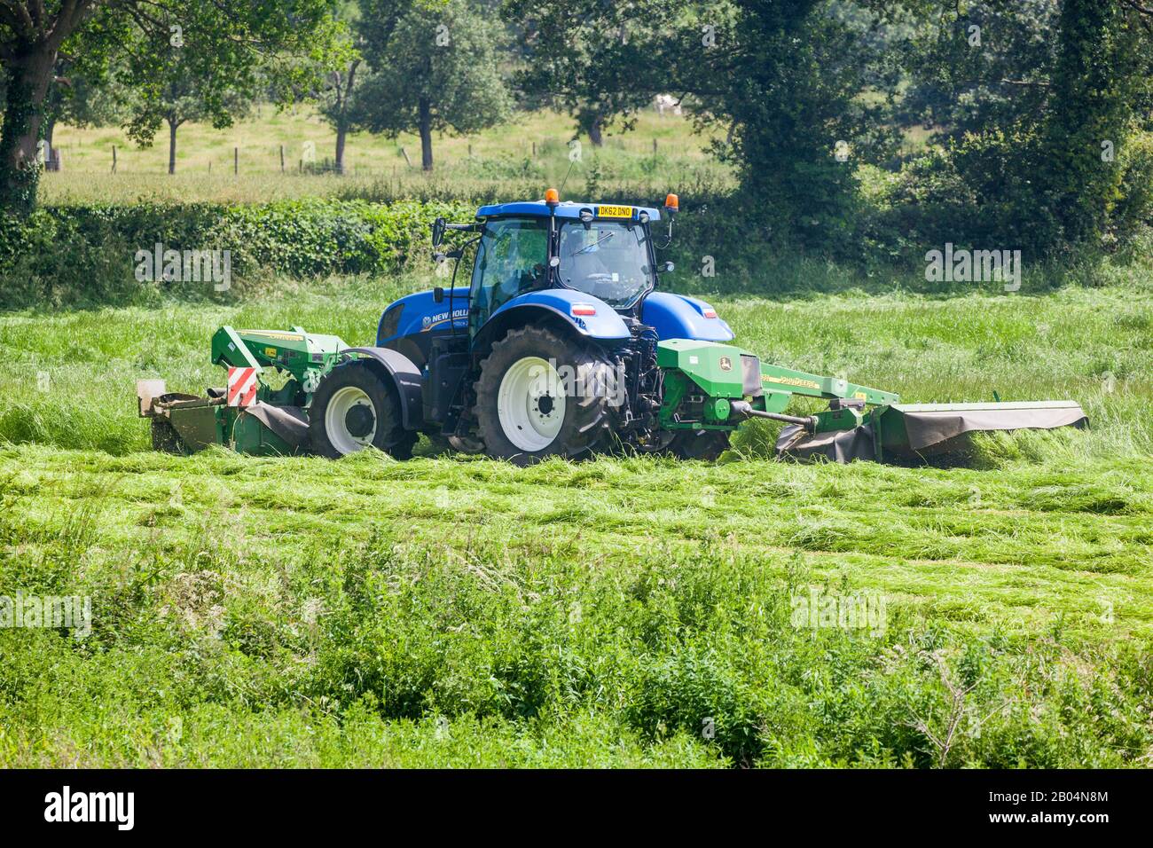 Agriculteur conduisant tracteur à couper l'herbe pour l'ensilage dans les terres agricoles du Cheshire Angleterre Royaume-Uni Banque D'Images