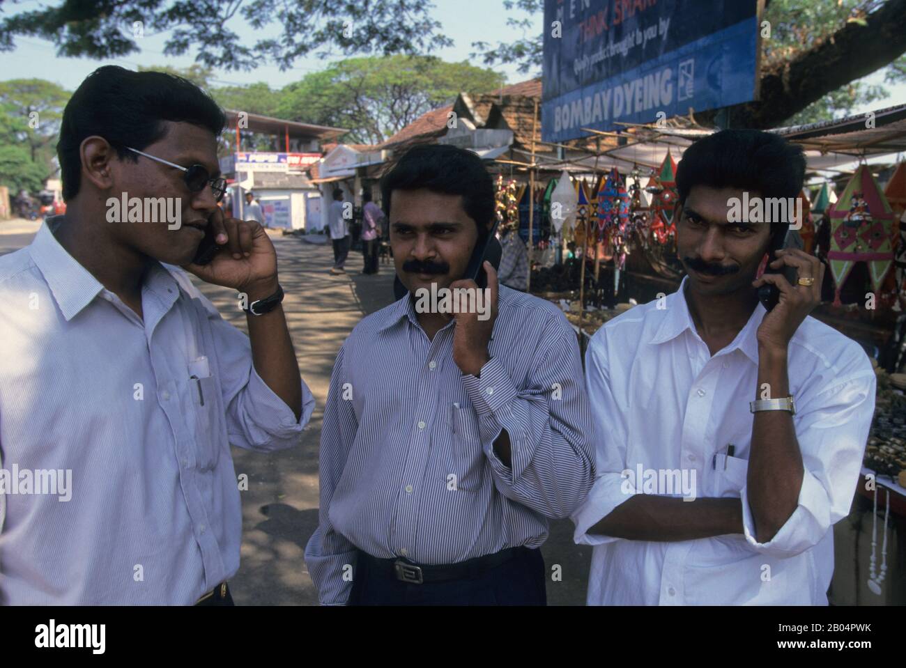 Trois hommes de la région qui font des appels téléphoniques sur une rue dans la ville de Jew de Cochin en Inde. Banque D'Images