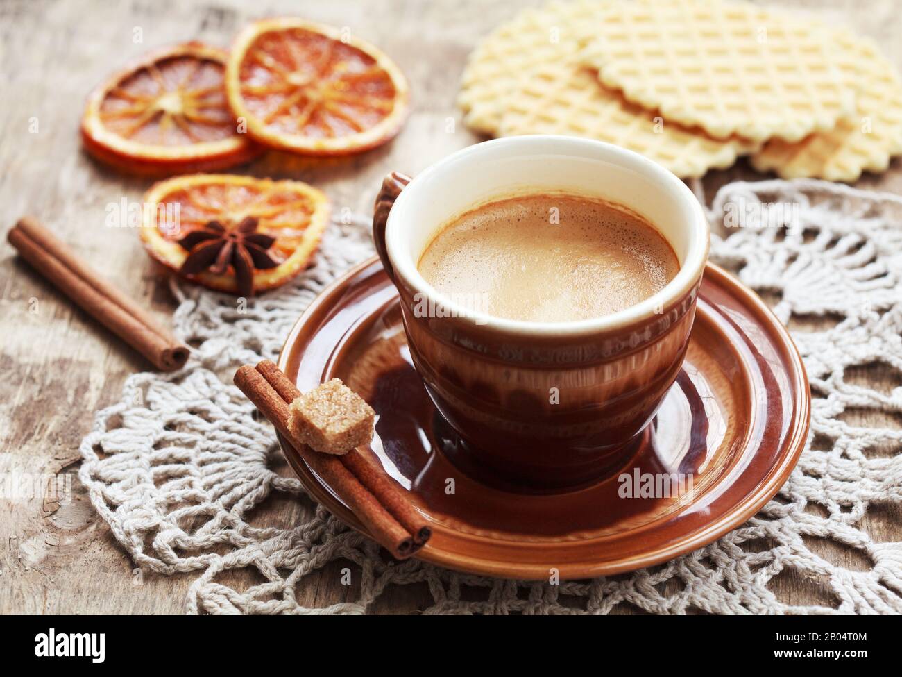 Une tasse de café, dentelle doily, orange confite, gaufres et bâtons de cannelle sur table en bois, style rustique. Mise au point sélective sur le café et les tons Banque D'Images