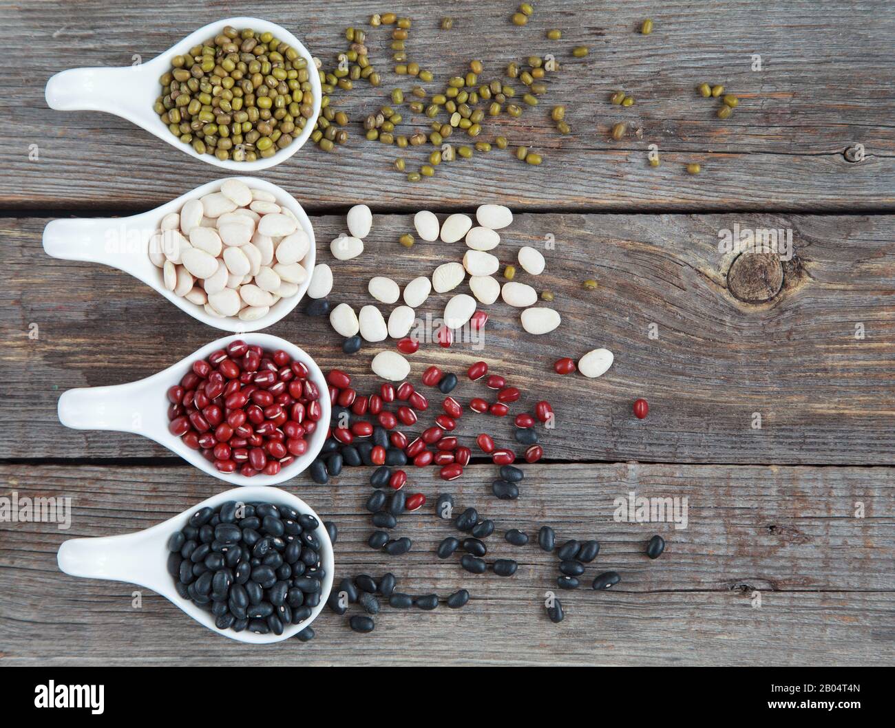 Ensemble de différentes variétés de haricots: Lima de bébé, petite noire, adzuki et mung dans des cuillères en céramique blanche (hors-d'œuvre) sur fond de bois, foc sélectif Banque D'Images