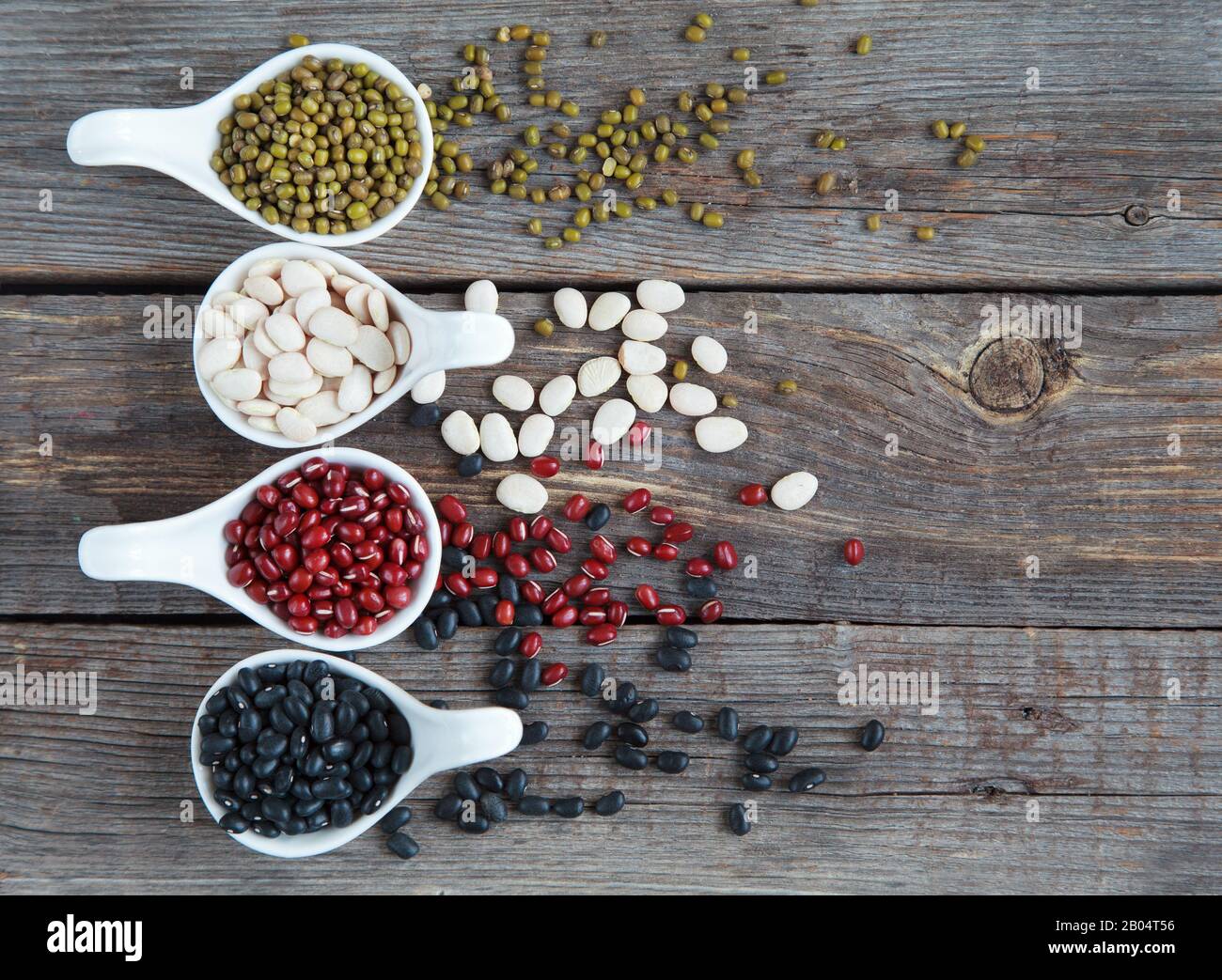 Ensemble de différentes variétés de haricots: Lima de bébé, petite noire, adzuki et mung dans des cuillères en céramique blanche (hors-d'œuvre) sur fond de bois, foc sélectif Banque D'Images
