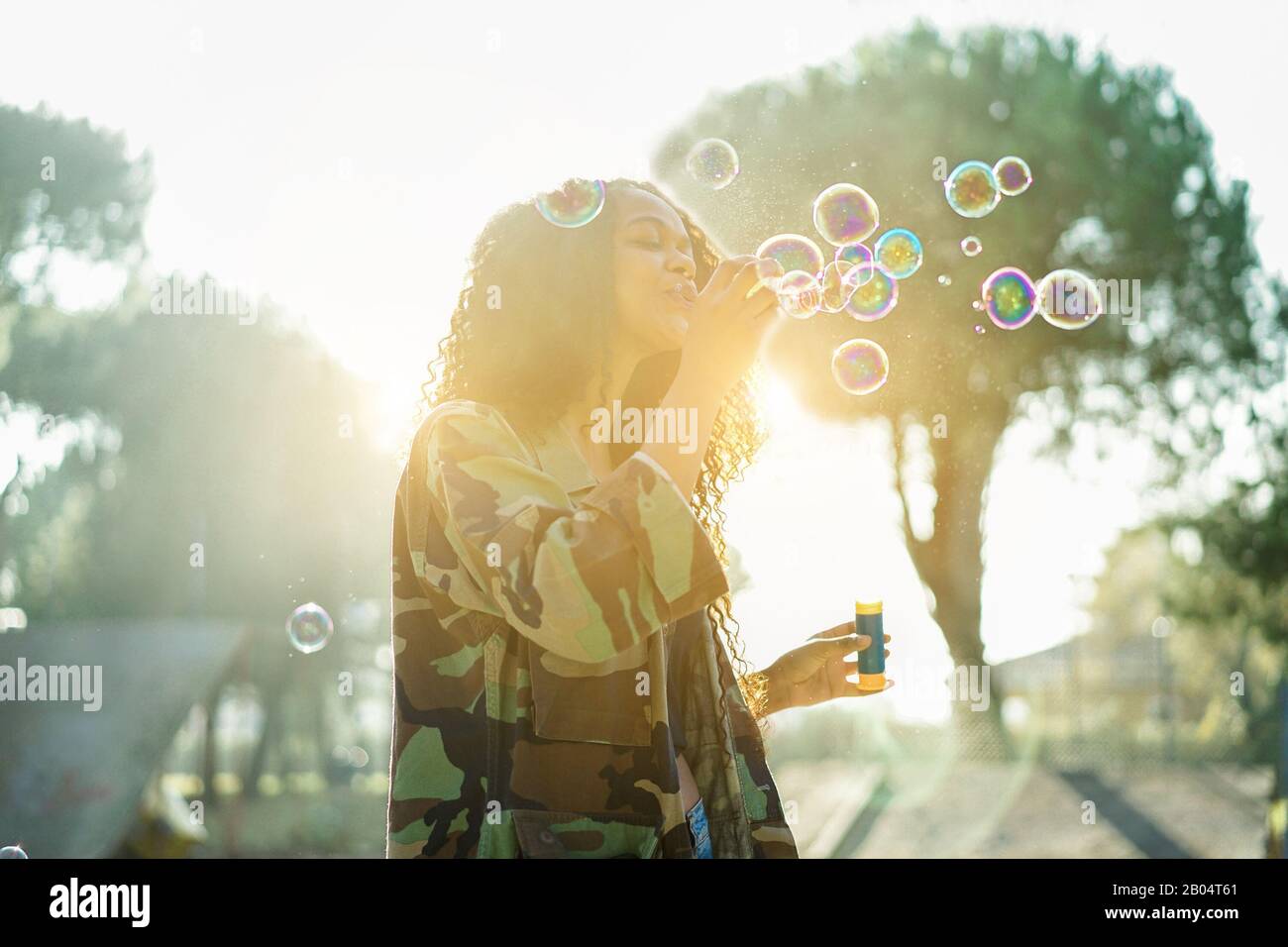 Jeune afro cheveux femme soufflant bulle de savon dans le parc de skate de ville avec le soleil arrière lumière - Portrait de fille africaine heureuse ayant plaisir en plein air - bonheur conce Banque D'Images