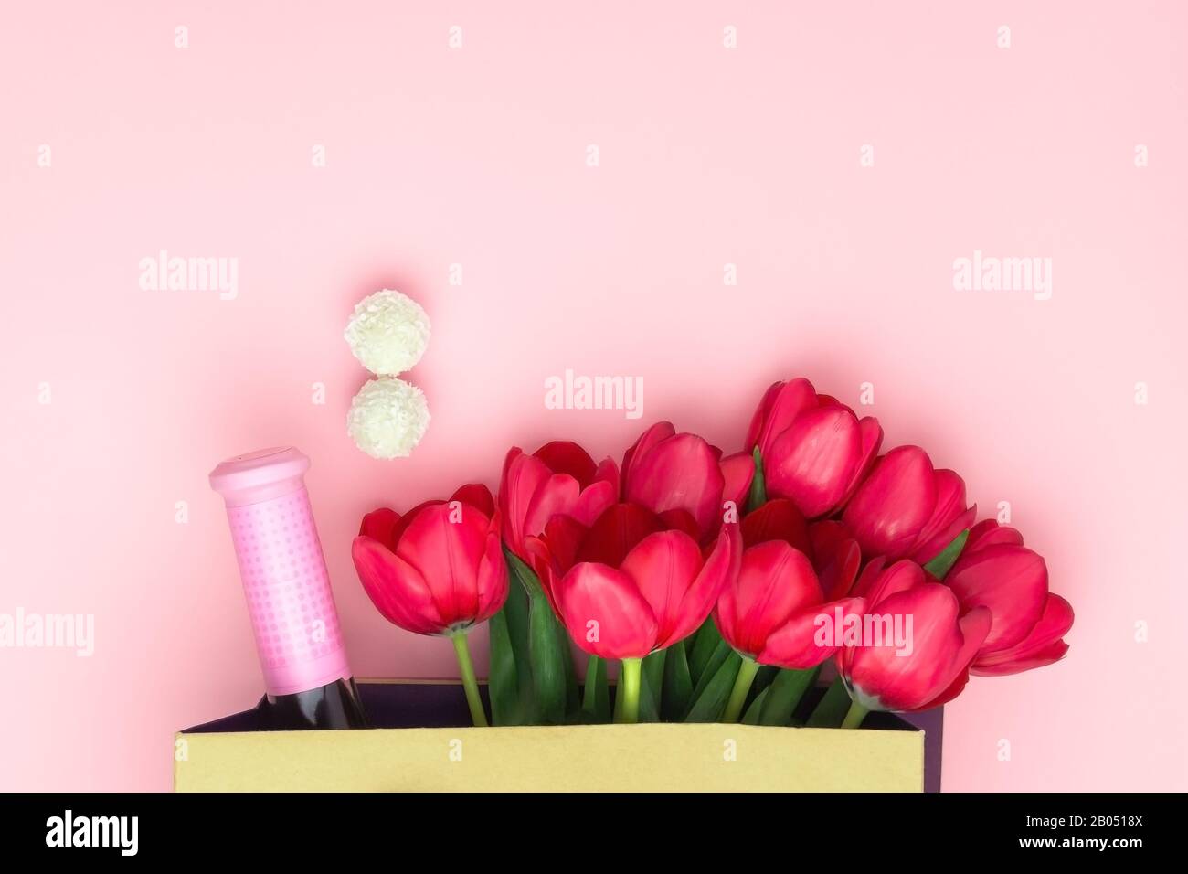Concept du présent avec du vin et des tulipes rouges dans le sac en papier sur le fond rose. Couche plate, vue supérieure, espace de copie. Journée femme, fête Des Mères Banque D'Images