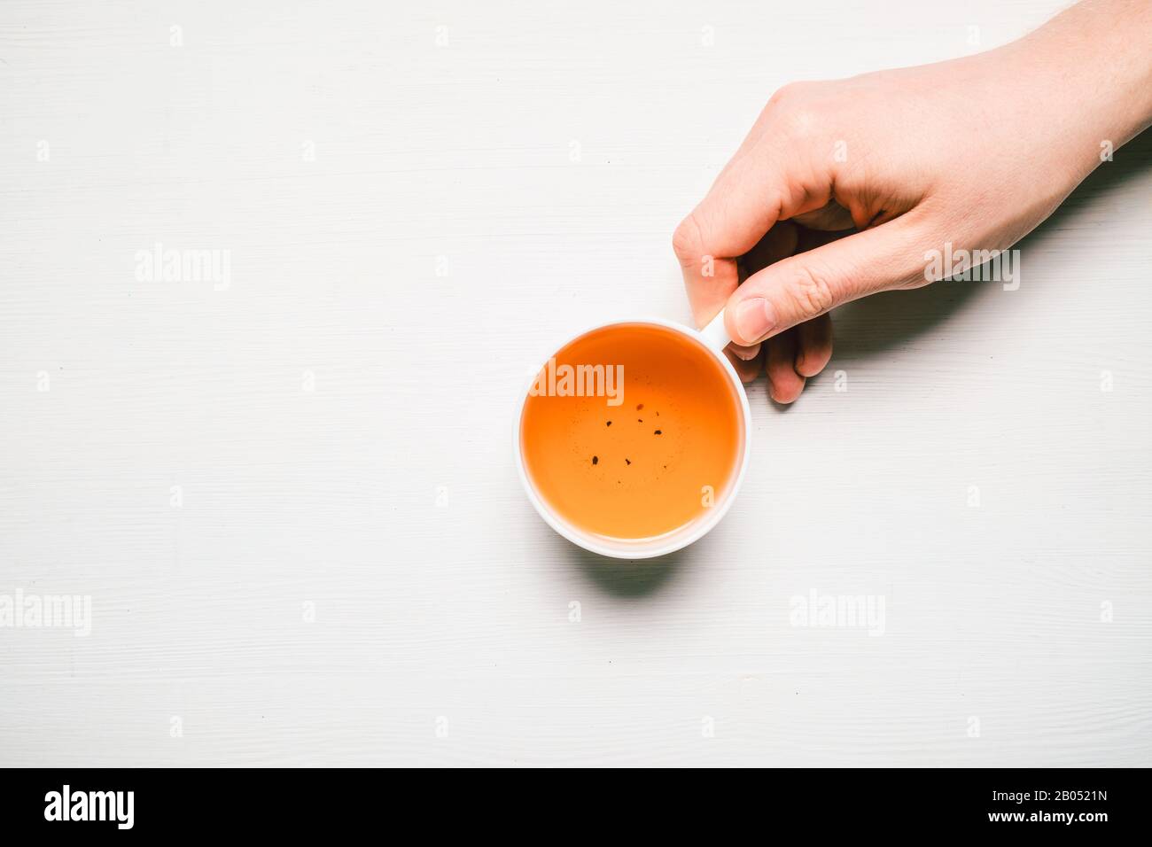 La main de l'homme tient un mug avec thé sur un fond en bois blanc avec espace de copie. Vue de dessus. Coose vers le haut. Banque D'Images