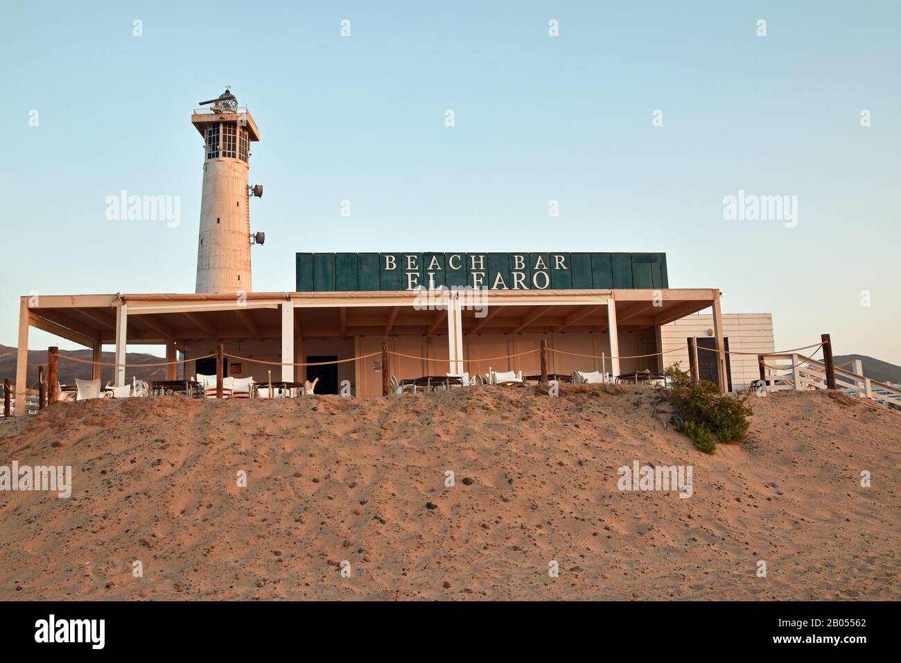 Beach Bar El Faro (le phare bar de plage) avec phare en arrière-plan. Pris au lever du soleil avec ciel bleu doux et aucune personne. Sable en premier plan. Banque D'Images