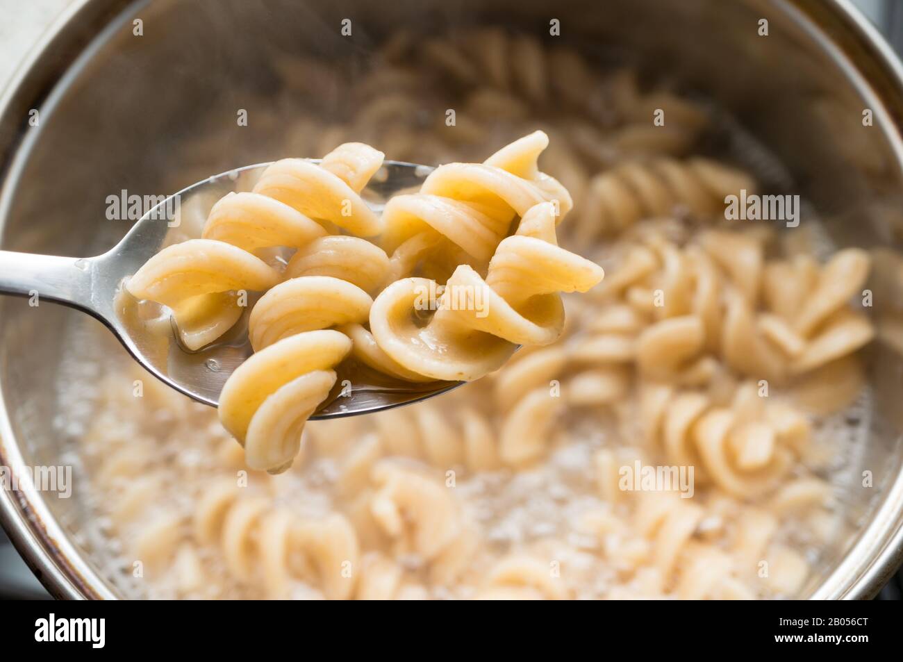Une cuillère avec fusilli de grain entier sur fond de pâtes, cuite dans une casserole. Saine alimentation. Banque D'Images