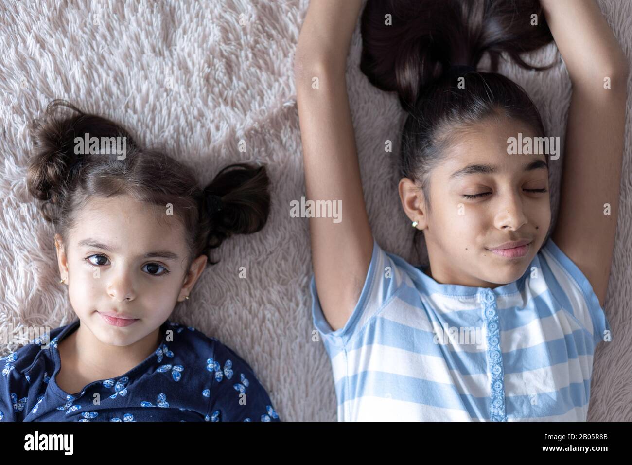 Deux jeunes filles noires, sœurs, se trouvent au lit dans une embrasse sur le dos. Des filles persanes sur le lit avec un téléphone. Enfants du Moyen-Orient. Banque D'Images