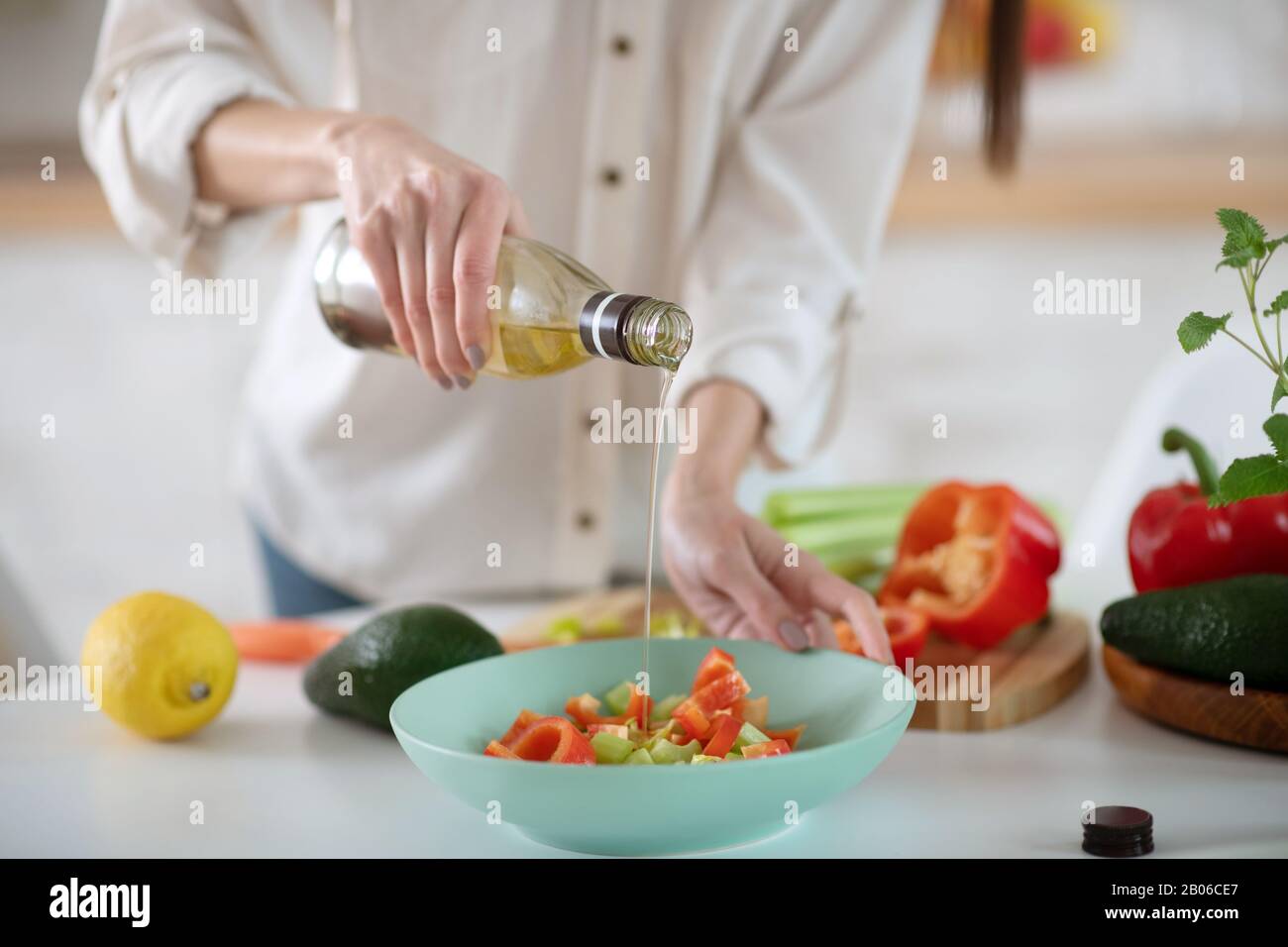 Mains d'une jeune femme qui verse de l'huile d'olive dans une salade. Banque D'Images