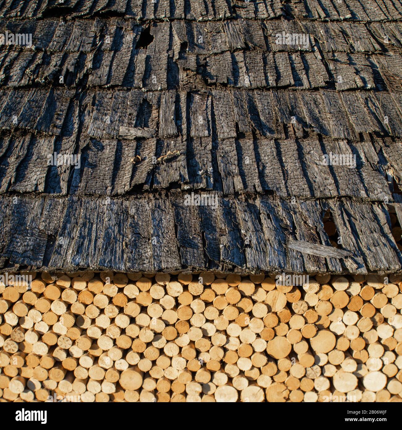 Bois dans une pile de bois, empilé sous un vieux toit en tuiles de bois. Banque D'Images