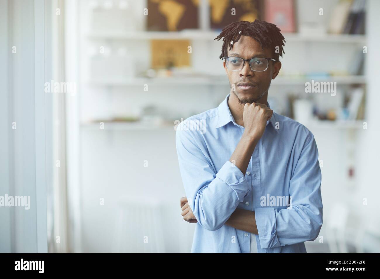 Homme d'affaires africain pensif dans les lunettes se tenant au bureau et regardant il pense à quelque chose Banque D'Images