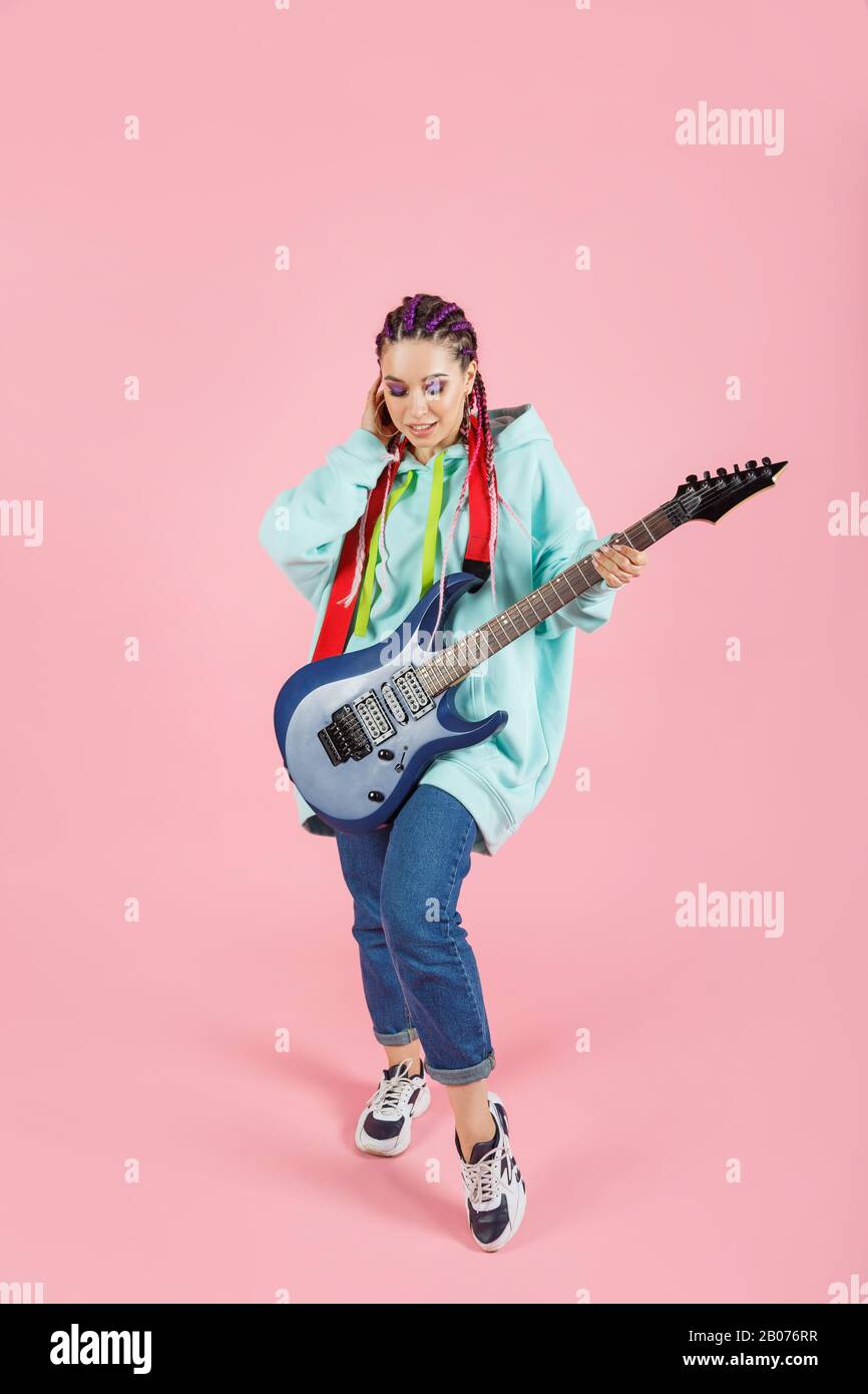 Jeune femme en vêtements surdimensionnés avec guitare électrique isolée sur fond rose Banque D'Images