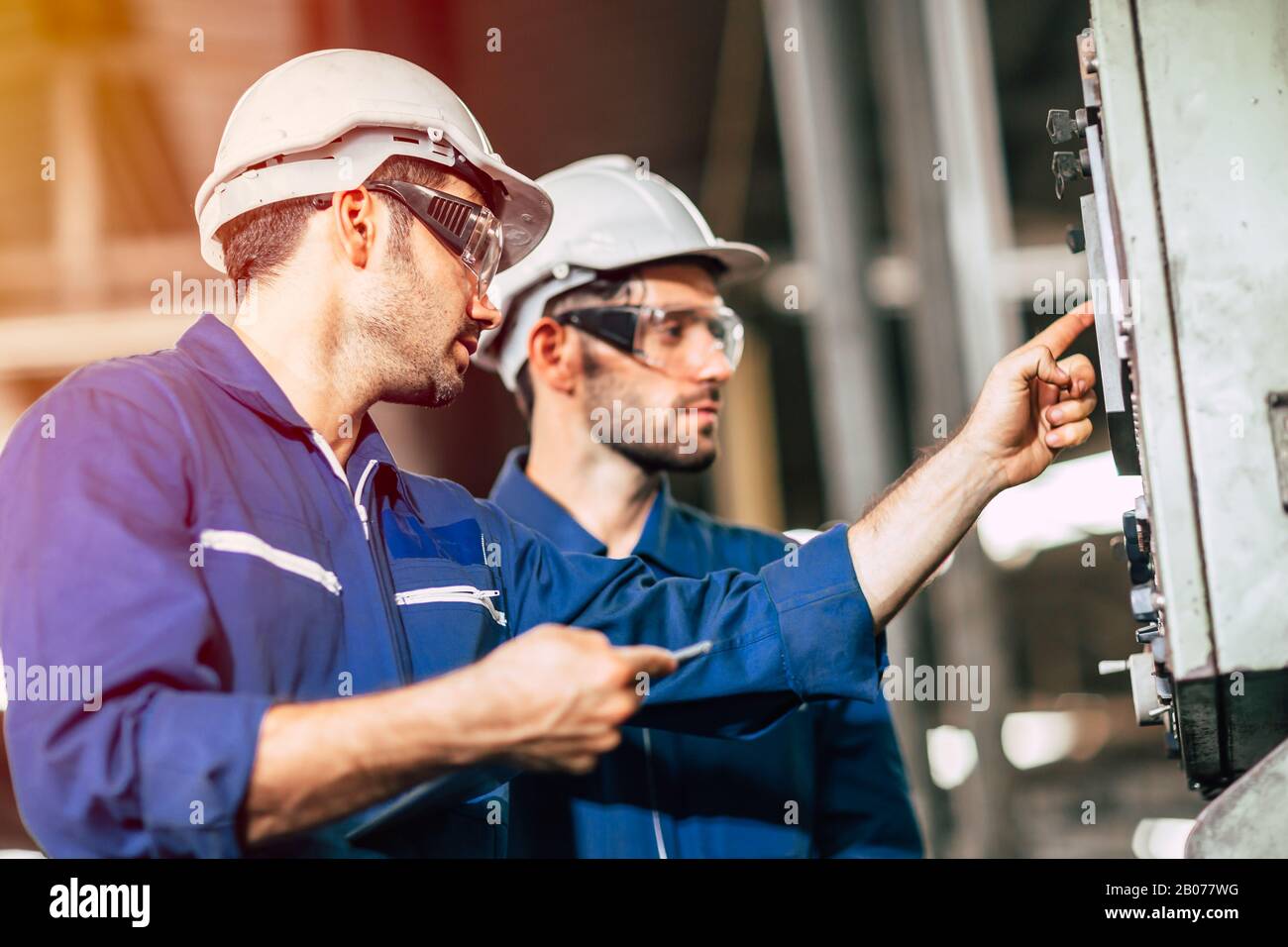 l'équipe d'ingénieurs de l'industrie qui enseigne aide un ami à utiliser la machine lourde de contrôle en usine Banque D'Images