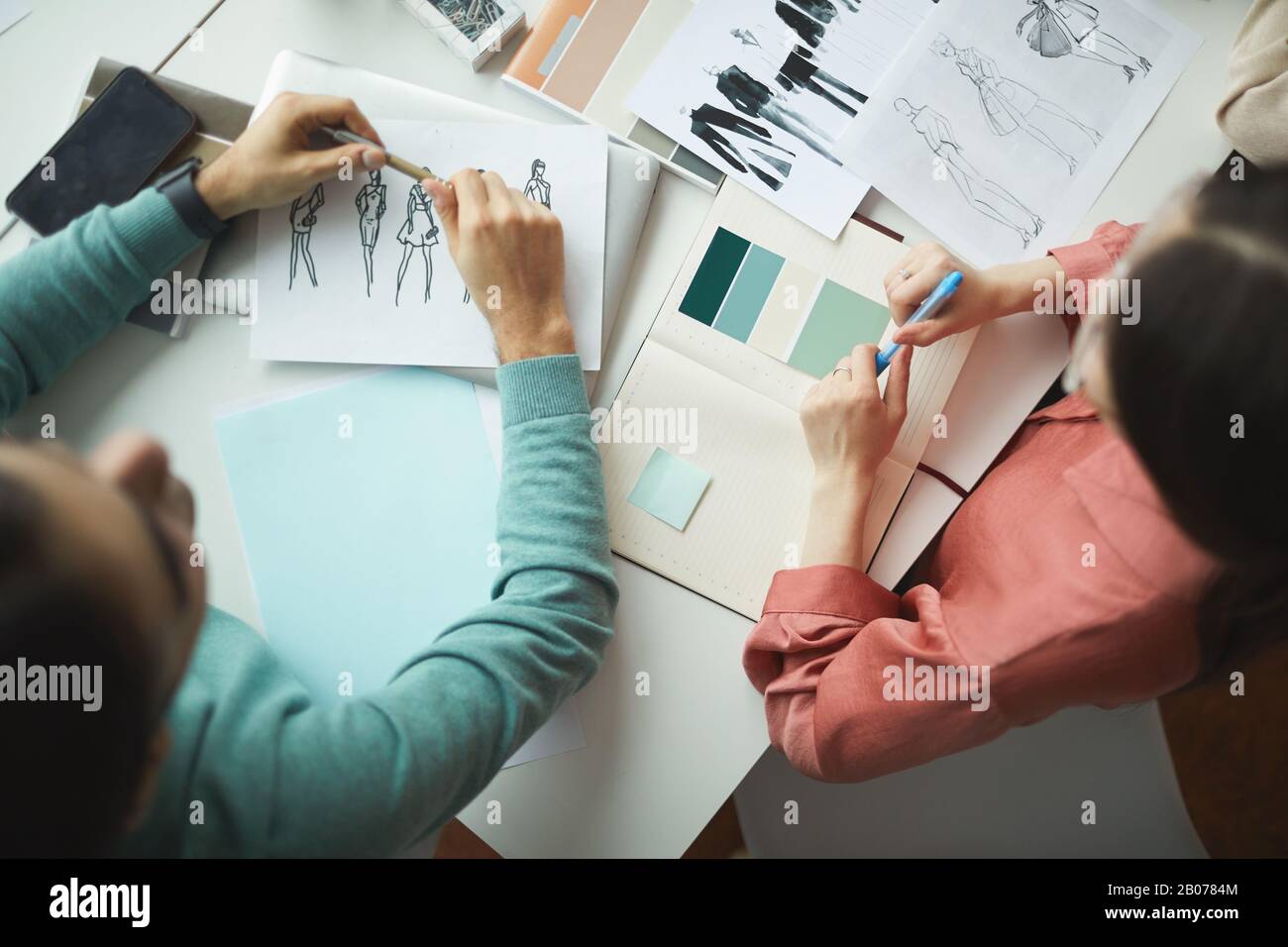Vue en grand angle de deux concepteurs travaillant avec des croquis de mode de vêtements et en discutant ensemble pendant une réunion Banque D'Images