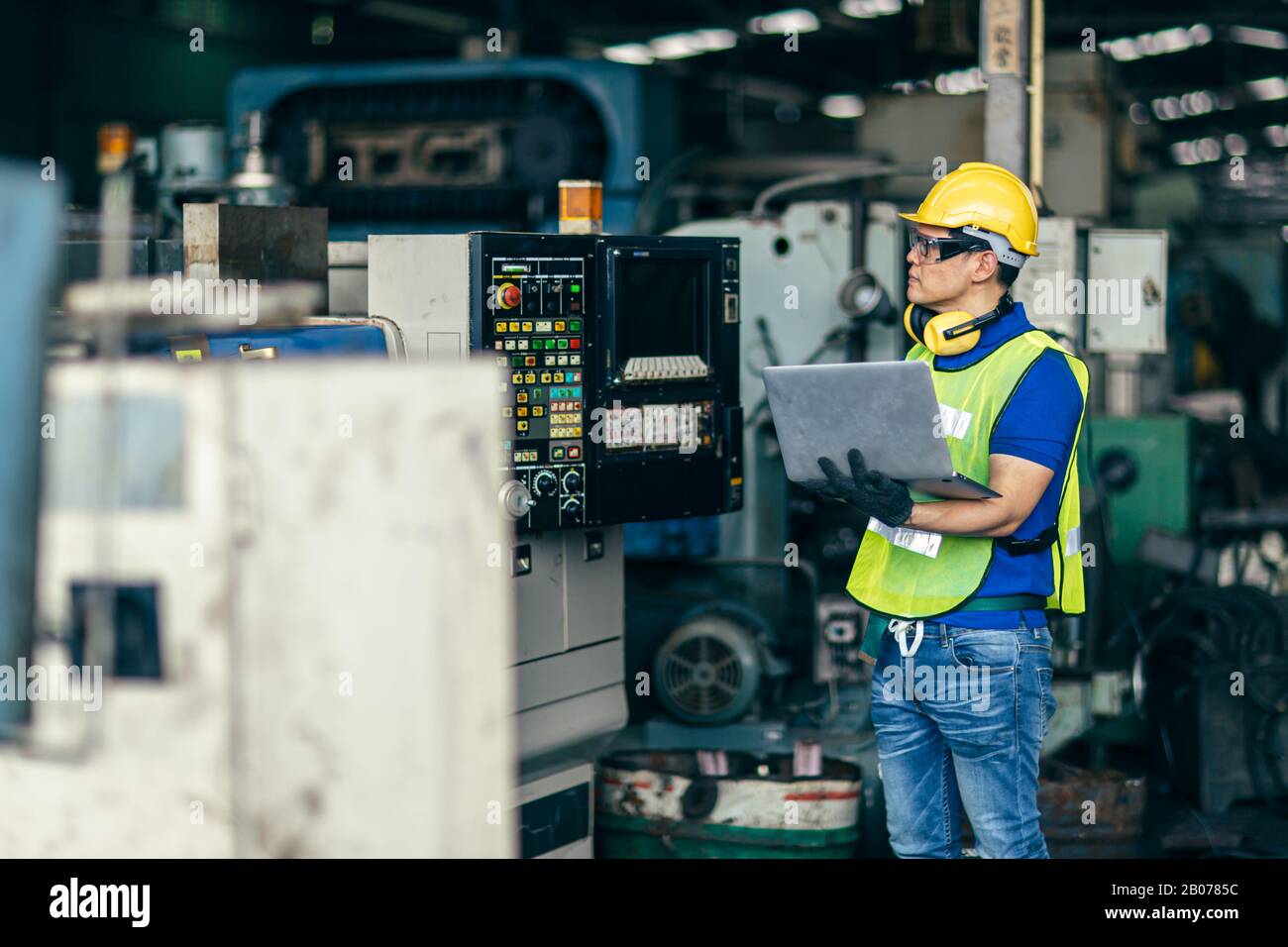 Un ingénieur asiatique programmant la machine en usine avec un ordinateur portable pour configurer le processus du programme. Banque D'Images