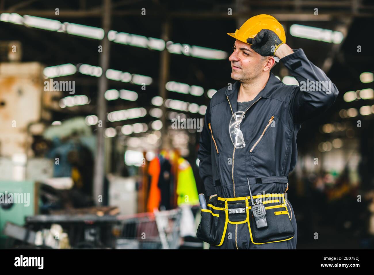 Travailleur heureux, portrait beau travail avec des outils de sécurité ceinture et radio service homme en usine. Banque D'Images