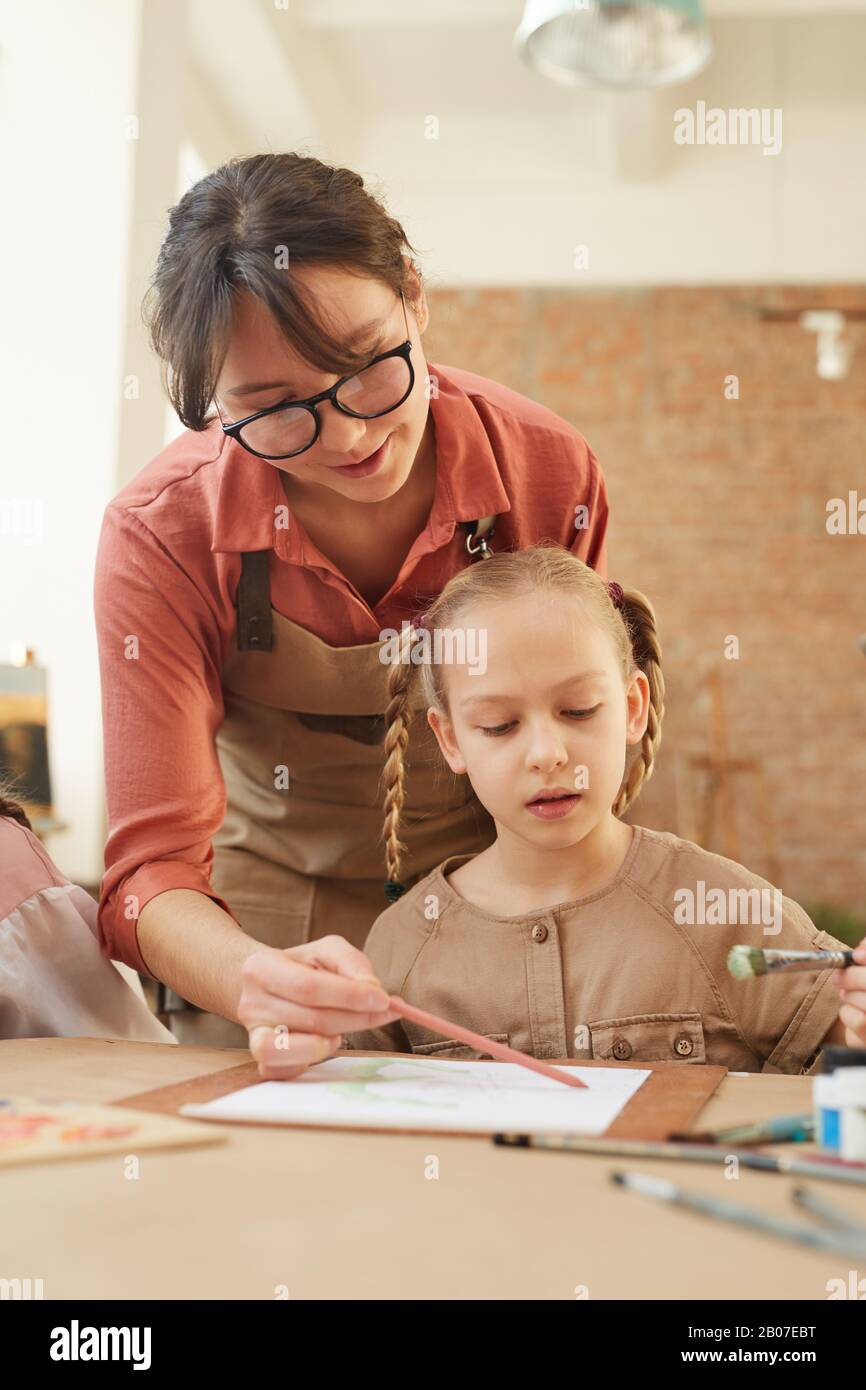 Jeune femme tenant le pinceau et aidant la petite fille à peindre pendant une leçon Banque D'Images