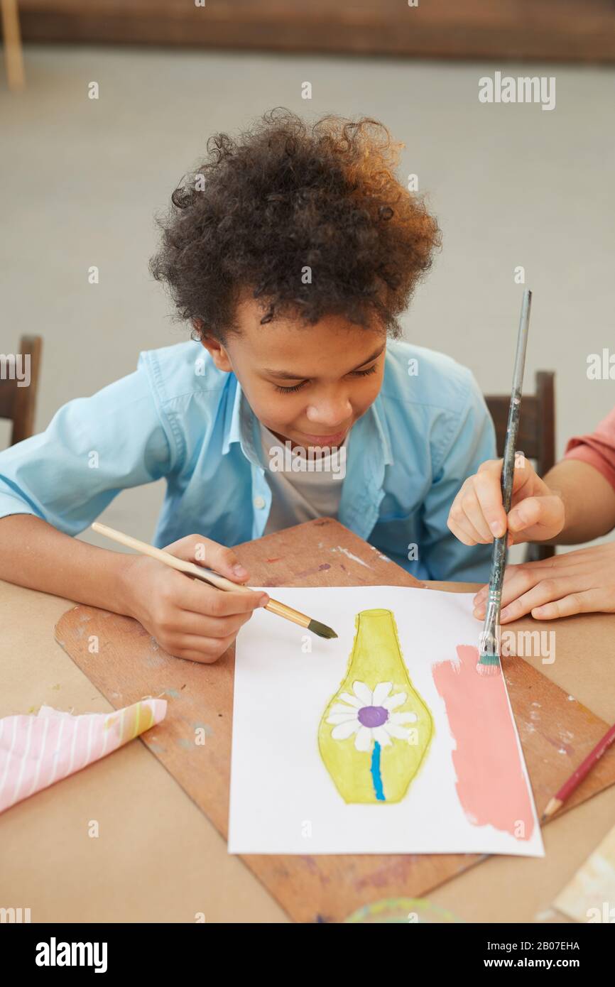 Jeune garçon africain assis à la table et peindre une image avec des peintures pendant la leçon d'art Banque D'Images