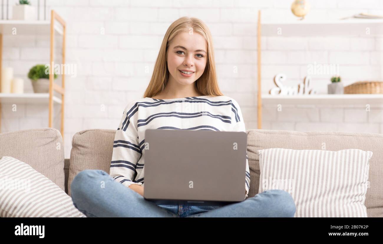 Jeune femme souriante avec ordinateur portable assis sur le canapé Banque D'Images