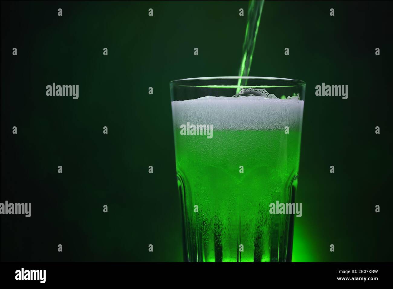Verser la bière verte dans le verre à bière sur fond sombre la nuit St patrick's Day Party avec espace de copie pour vous faire de la publicité design backdrops Banque D'Images