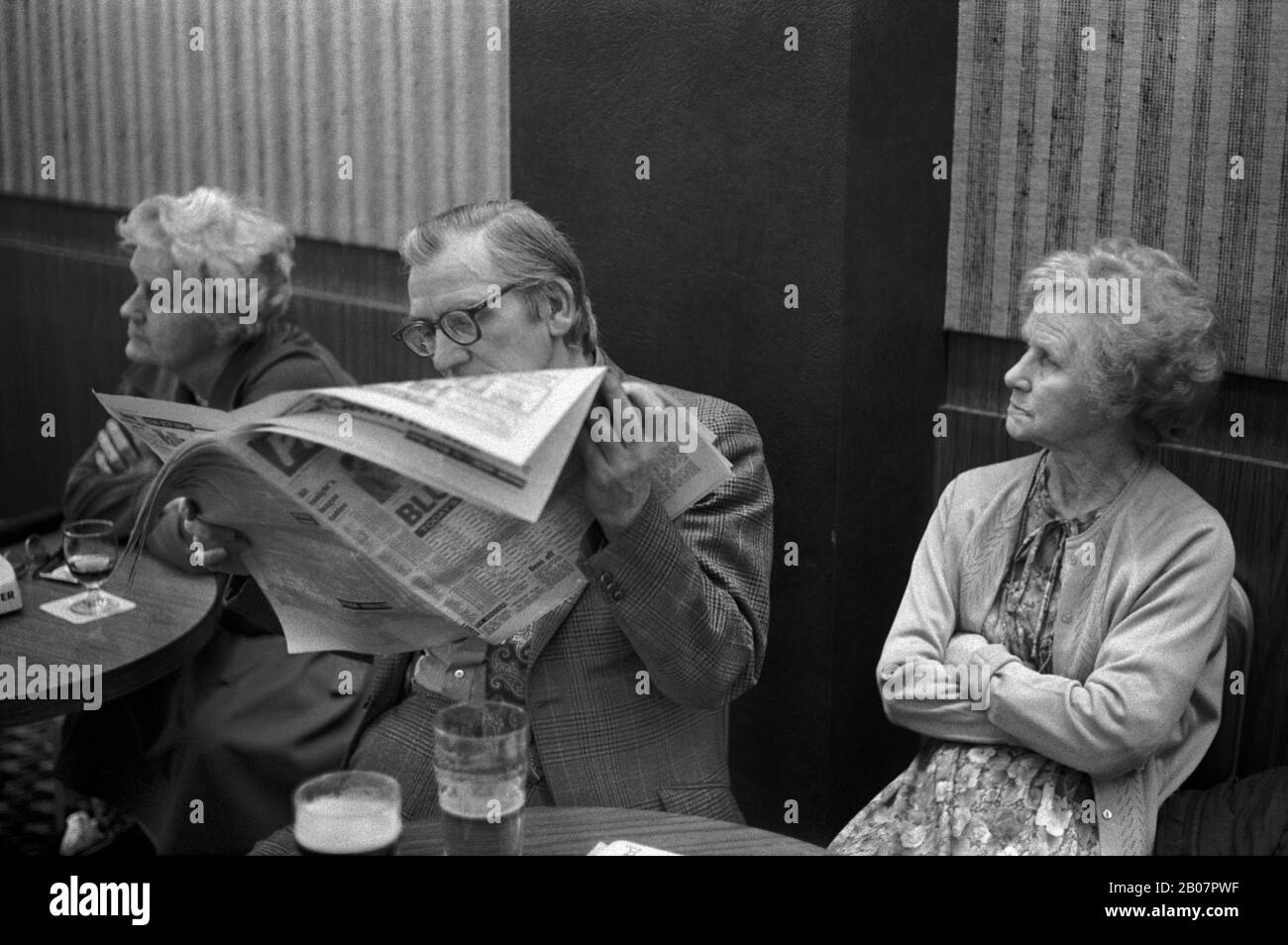 Couple ennuyé, homme lisant un journal ignorant sa femme. Le club des hommes en activité est le samedi soir après les animations du soir de Bingo. 1980 Coventry Angleterre. SYSTÈMES HOMER Banque D'Images