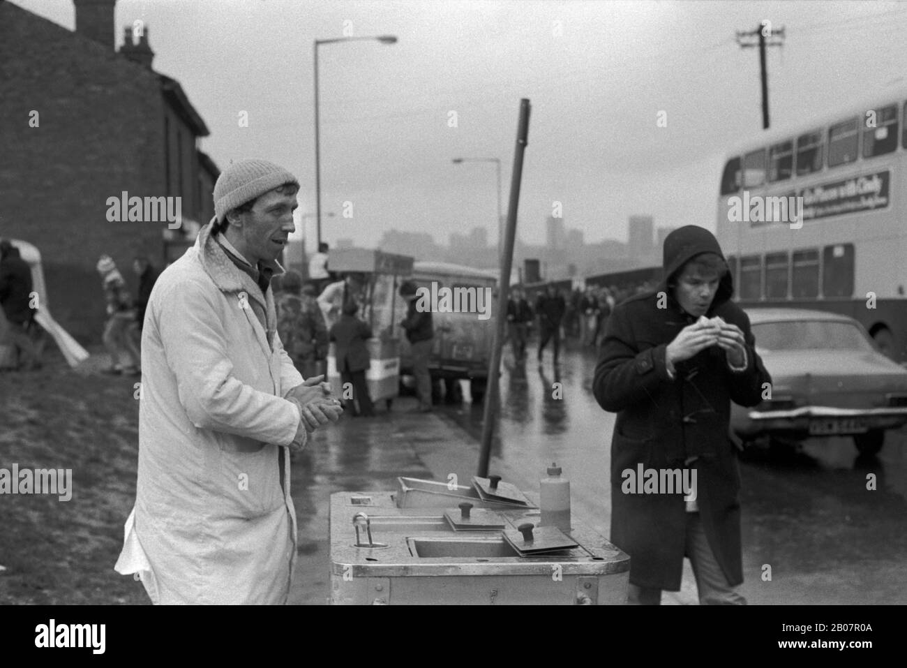 Rentrer à la maison par mauvais temps, vendeur de fast food et jeune homme en duffle coat mangeant une collation. Départ du match de football de Coventry City, au Highfield Road Stadium. Circa mars 1981 1980s Royaume-Uni. HOMER SYKES Banque D'Images