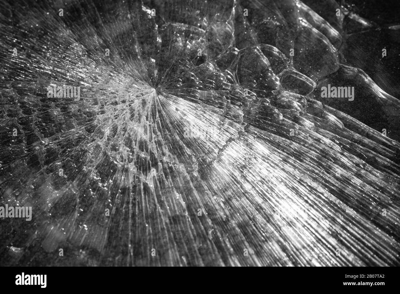 Texture abstraite d'une feuille de verre cassée sur fond de pierre sombre. Photo en noir et blanc Banque D'Images