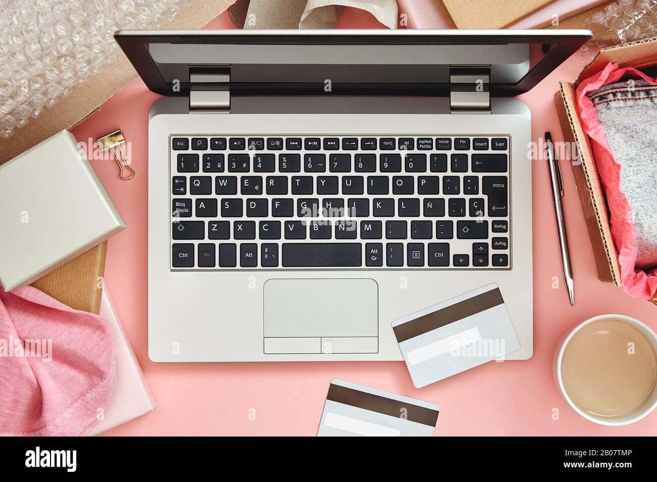 Concept de shopping en ligne sur table de bureau rose avec ordinateur portable, cartes de crédit, colis et vêtements. Vue de dessus. Banque D'Images