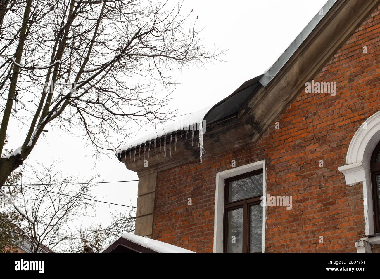 Glaces sur le bord du toit d'une maison en briques. Hiver, glace sur le toit. Maison de campagne en brique rouge avec toit enneigé, icicules danger W Banque D'Images