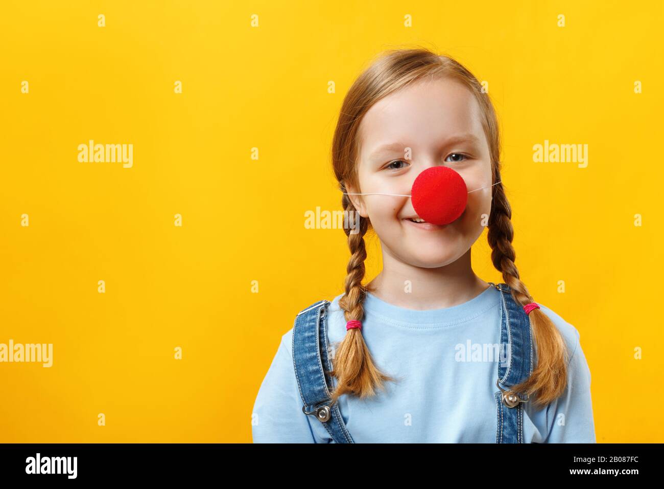 Heureux drôle enfant clown avec un nez rouge. Petite fille gaie sur un fond jaune. 1 avril Journée de l'imbécile. Espace de copie. Banque D'Images