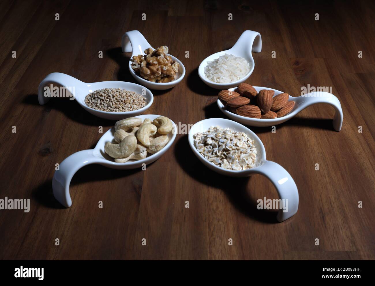 Ingrédients pour Le Lait de légumes pour l'auto-production, disposés sur une plaque en bois dans des bols blancs, amandes, noix, riz, flocons d'avoine, noix de cajou, sesams Banque D'Images