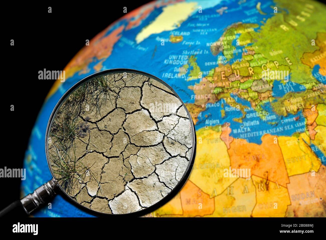 La terre craquelée par la sécheresse vu à travers une loupe tenu contre allumé globe terrestre Banque D'Images