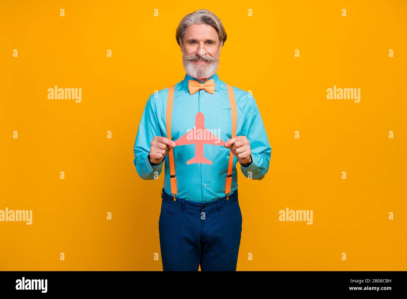 Photo de cool élégant grand-pa tenir papier avion recommander choisir nouveau transport aérien porter chemise bleue bretelles noeud cravate pantalon isolé Banque D'Images