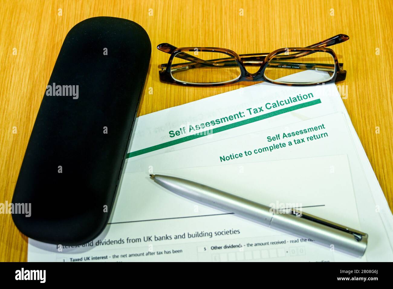 Vue rapprochée d'un formulaire de déclaration de taxe auto-évaluation sur une table en bois avec un stylo, une paire de lunettes et un étui pour lunettes Banque D'Images