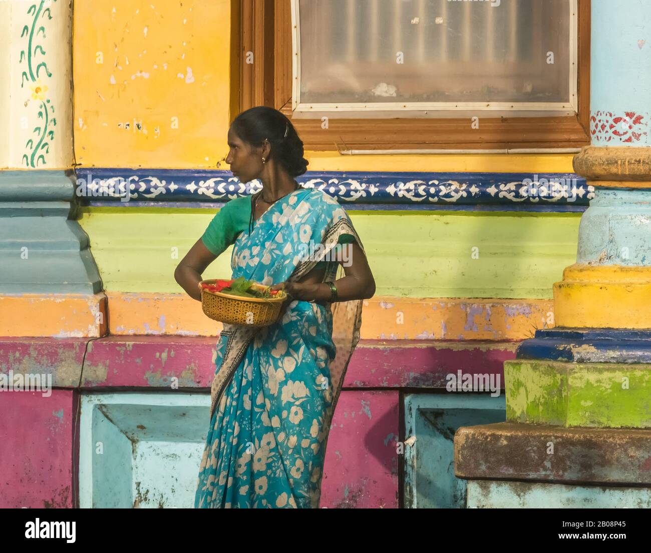 Un portrait de rue candide d'une femme tenant un panier de fleurs à l'extérieur des murs colorés d'un vieux temple. Banque D'Images